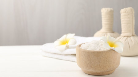 Sea salt in bowl, plumeria flowers, herbal bags and towels on white wooden table, closeup. Space for textの写真素材