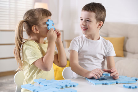 Little brother and sister playing with puzzles at white table indoorsの写真素材