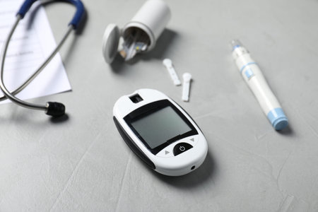 Diabetes. Digital glucometer, pen, lancets, stethoscope and record form on gray textured table,...