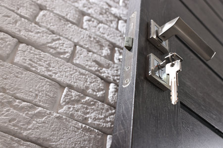 Wooden door with keys and metal handle near white brick wall, low angle view. Space for text