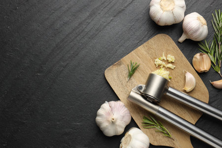 Fresh garlic, press and rosemary on black table, flat lay. Space for textの写真素材