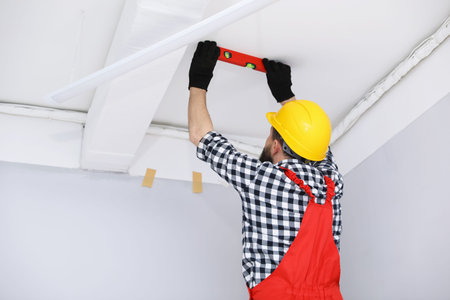 Worker measuring ceiling with building level indoors, back viewの写真素材