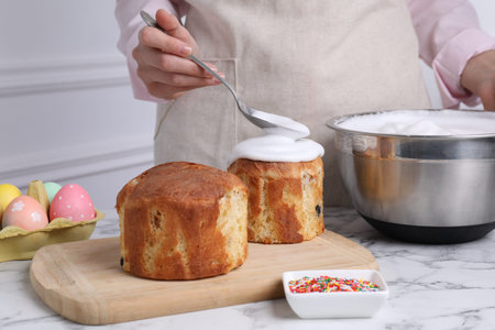 Woman decorating traditional Easter cake with glaze at white marble table indoors, closeup