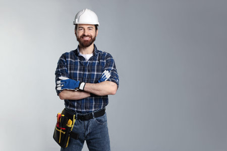 Professional builder wearing hardhat and tool belt on light gray background. Space for text