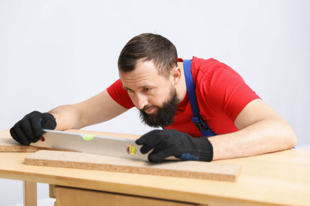 Worker measuring wooden plank with building level at table indoors
