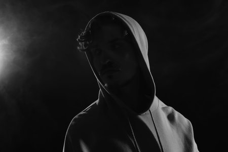 Man in hood on dark background with smoke. Black and white effect