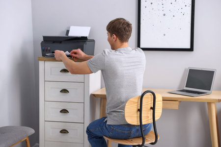 Man taking printed sheet of paper from printer at desk indoors, back view