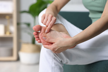 Woman doing foot massage herself on sofa indoors, closeup. Space for text