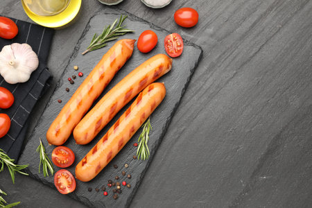Grilled sausages, tomatoes and spices on black table, flat lay. Space for textの写真素材