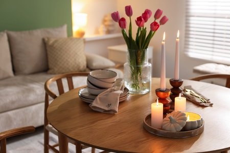 Beautiful candles, tulips and dishware on wooden table at home