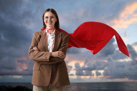 Businesswoman wearing cape against seascape at sunsetの写真素材
