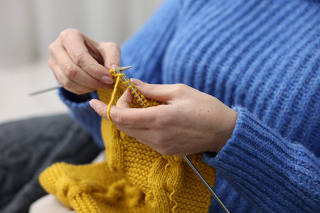 Senior woman knitting with needles on sofa at home, closeup