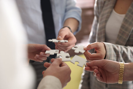 Teambuilding. Group of businesspeople putting puzzle pieces together indoors, closeup