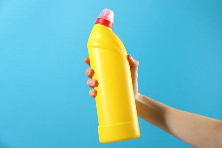 Woman with bottle of toilet cleaner on light blue background, closeup