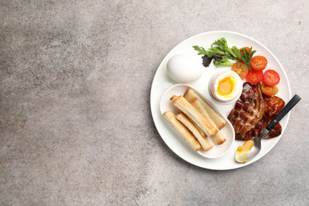 Tasty breakfast with soft boiled eggs, bacon, toasted bread and tomatoes on gray table, top view....