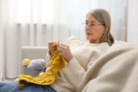 Senior woman knitting with needles on sofa at home