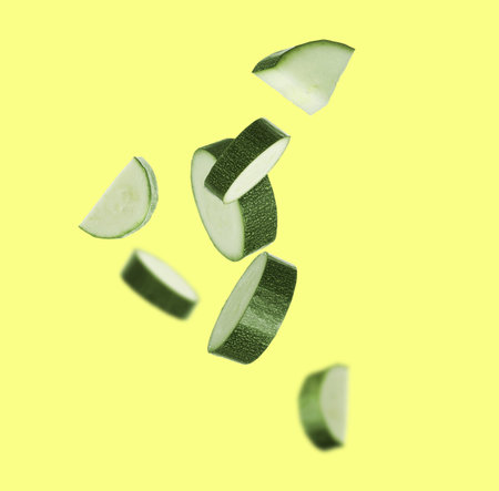 Zucchini pieces falling against yellow background. Fresh vegetablesの写真素材