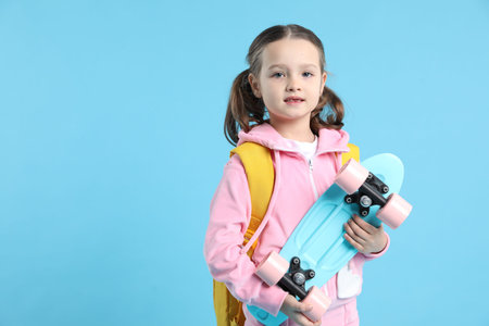 School holidays. Cute girl with backpack and penny board on light blue background, space for text