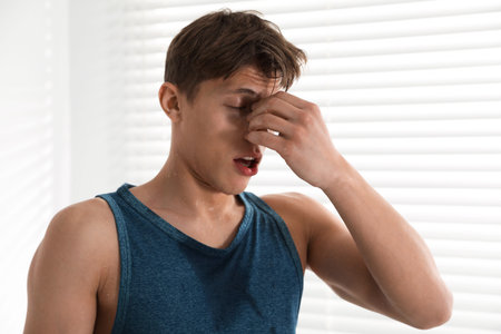 Young sportsman feeling fatigue near window at home