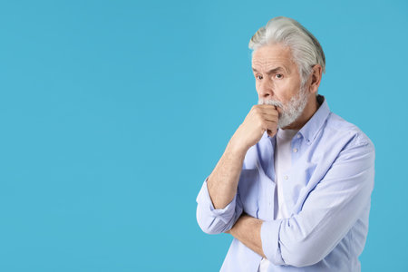 Senior man trying to remember something on light blue background, space for text