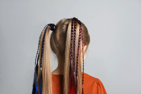 Little girl with colorful clip-in braids extensions on gray background