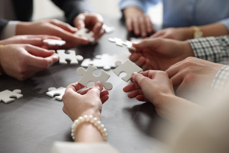 Teambuilding. Group of businesspeople solving puzzle together at dark wooden table against light...