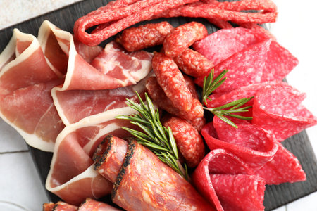 Charcuterie board with different cured meat and sausages on white tiled table, top view