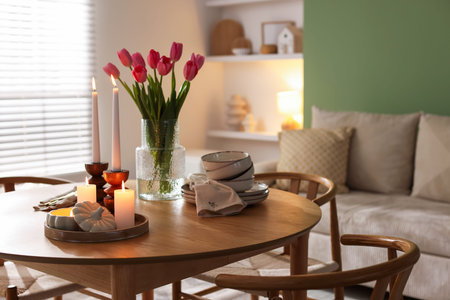 Beautiful burning candles, tulips and dishware on wooden table at home. Space for text