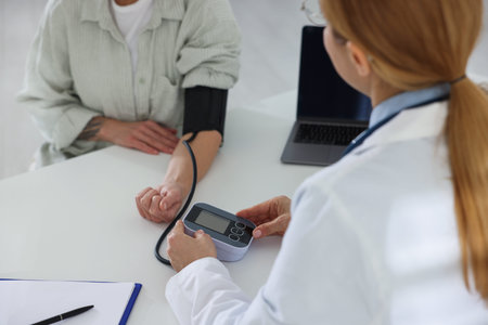 Cardiologist measuring patient's blood pressure at white table in hospital, closeup