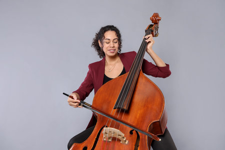 Woman playing double bass on gray background
