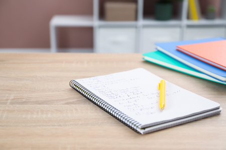 Homework. Notebook with math exercise and pen on wooden desk, closeup. Space for text