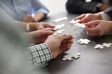 Teambuilding. Group of businesspeople solving puzzle together at dark wooden table against light...