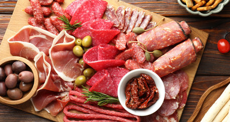 Charcuterie board with different cured meat, sausages and olives on wooden table, flat lay