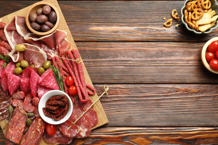 Charcuterie board with different cured meat, sausages and olives on wooden table, flat lay. Space...
