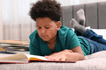 Boy reading book on bed at homeの写真素材
