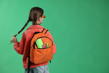 Schoolgirl with backpack on green background, space for text