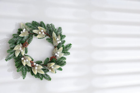 Beautiful Christmas wreath on white wall, space for text