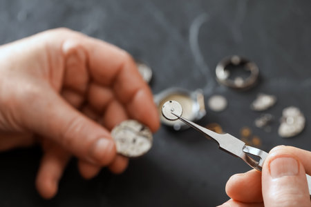 Senior man fixing mechanism of vintage wrist watch at black table, closeup