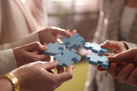 Teambuilding. Group of businesspeople putting puzzle pieces together indoors, closeup