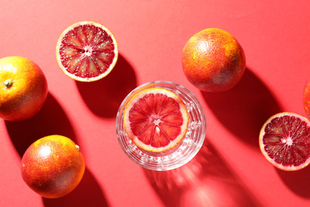 Refreshing drink in glass and Sicilian oranges on red background, flat lay