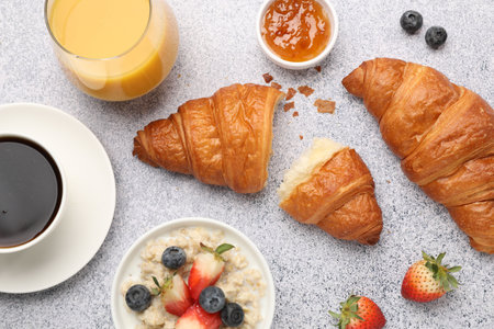 Yummy breakfast. Tasty croissants, jam, berries, oatmeal and drinks on light gray table, flat lay