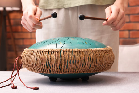 Woman playing steel tongue drum with mallets at gray table indoors, closeup
