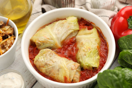 Delicious stuffed cabbage rolls in bowl and ingredients on table, closeup