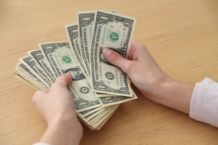 Woman counting dollar banknotes at wooden table, closeup