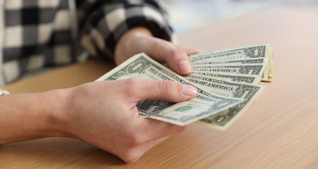 Woman counting dollar banknotes at wooden table, closeup