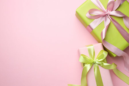 Wrapped gifts with bows on light pink background, flat lay. Space for text