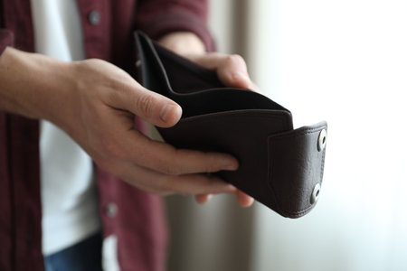 Man holding empty wallet against blurred background, closeup