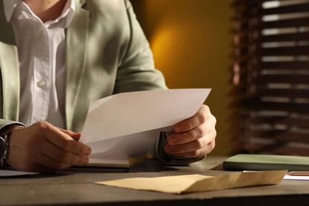 Man reading letter at wooden table indoors, closeup. Space for text