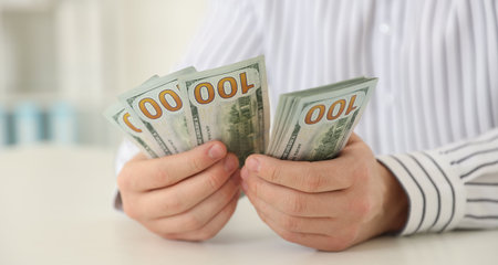 Man counting dollar banknotes at white table, closeup