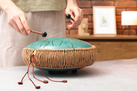 Woman playing steel tongue drum with mallets at gray table indoors, closeup